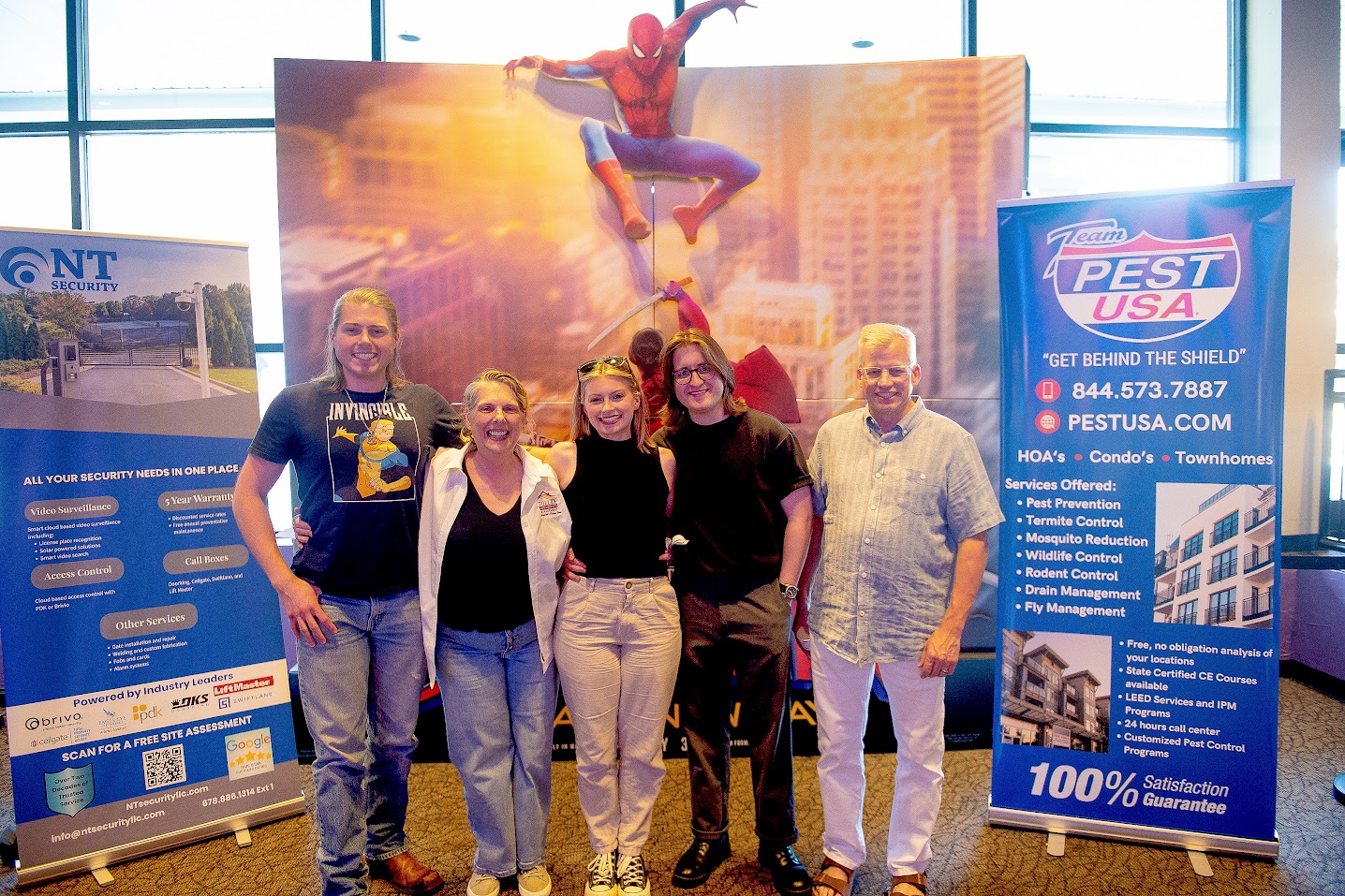 NT Security and Team Pest USA banners in the theater lobby at Family Movie Night in Atlanta, with guests posing in front of a Spider-Man: Brand New Day display